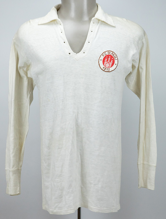 Original match-worn player shirt from FC St. Pauli Hamburg (Amateur team) from 1961. Worn by Peter Wagner in a league match. Includes original FC St. Pauli shorts. Status:ABA. Also included: FC St. Pauli "match call-up" postcard addressed to player Peter Wagner, postmarked February 16, 1961. Museum piece!! Long-sleeved shirt; size 6; cotton; manufacturer: "WeBe" (embroidered label). Sewn-on, embroidered FC St. Pauli club crest. No number on the back (it was common practice for amateur players to play without back numbers!). Shorts: cotton in the signature St. Pauli brown. Size: 5. Manufacturer: Allround (embroidered label). Very well-preserved items; rarely found in this condition! --The shirt comes directly from the estate of player Peter Wagner. Condition: A-