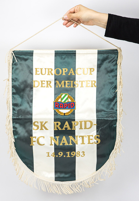 Wien,Rapid  - Wimpel 1983  | Original Spielwimpel von Rapid Wien mit goldbeflockter Aufschrift „SK Rapid Wien - FC Nantes 14.9.1983“ (3:0; Rückspiel 1:3) mit aufgesetztem, farbig besticktem Vereinslogo. Zweifarbiger Seidenwimpel mit weißer Seidenkordel und weißen Seidenfransen. 53x43 cm. Es handelt sich hier um den Wimpel den der Mannschaftskapitän des FC Nantes Maxime Bossis im Mittelkreis erhalten hat.