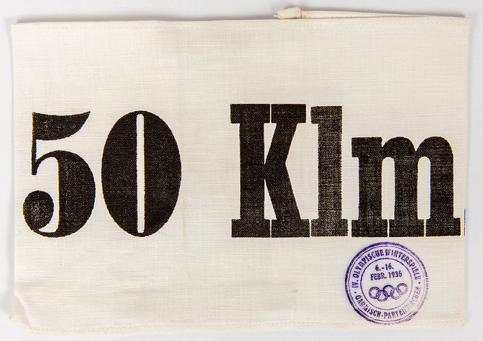 Olympic Games 1936 Skiing: Official Bib - Official Cross Country Skier's bib from the Olympic Winter  Games 1936. With original Olympic 1936 stamp,  white cloth, with  black lettering " 50Km." and original bands. Size 16.5x11.5cm. EF. Condition: A