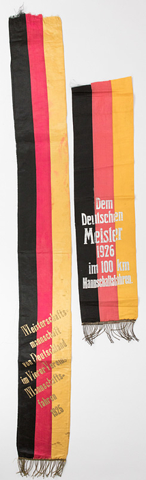 Meisterscherpe Radsport 1926  | 2 Meisterscherpen der DRU (Deutscher Radfahrer Union): 1) "Dem Deutschen Meister 1926 im 100 km Mannshaftsfahren" (nur halbe Scherpe vorhanden; Sieger RV Concordia Hannover ). 2) "Meistermannschaft von Deutschland im Vierer Vereins Mannschaftsfahren 1925" (Sieger RV Triumph Braunschweig).  Beide Kreppstoff mit silber- bzw. goldbedruckter Aufschrift. Goldbrokatfransen. 104x13 + 61x16,5 cm