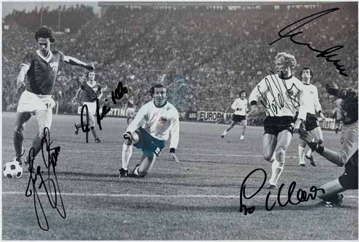  - World Cup 1974: Large photographic print of the match between West Germany and East Germany at the 1974 World Cup in Hamburg, capturing the moment Jürgen Sparwasser scored the decisive goal (1–0) for East Germany. Features five original signatures from the players shown: Jürgen Sparwasser, Bernd Cullmann, Berti Vogts, Sepp Maier, and others. The photograph comes from the collection of Horst-Dieter Höttges (who did not sign it). 30 x 20 cm. Condition: A-