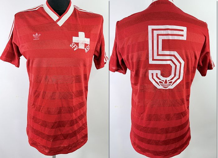  - Original match-worn Switzerland player shirt, number 5 (Alain Geiger). Worn in an international match in 1984. Short-sleeved shirt; size 7/8 (L); federation logo applied via wet flocking; manufacturer's logo applied as a rubberized transfer; back number applied via wet flocking; 38% cotton, 62% polyester; made in West Germany. Status:ABC Condition: A-