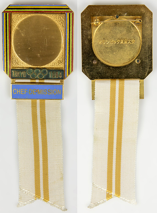 Teilnehmerabzeichen 1964  | Offizielles Teilnehmerabzeichen Tokyo 1964 „Chef de Mission“. Bronze, vergoldet, teilweise farbig emailliert. Schriftleiste hellblau emailliert. Weißes Seidenband mit zwei gold-gelben Streifen. 15x5,1cm.