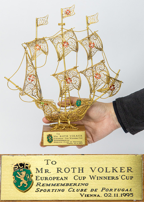 Lissabon,Sporting-Segelschiff 1995  | Ehrengeschenk an den Spielerbeobachter der UEFA Volker Roth von Sporting Lissabon anlässlich des UEFA-Europapokal-Spieles Rapid Wien v Sporting Lissabon (4:0) am 2.11.1995. Vergoldetes Segelschiff aus Kupfer auf einem Holzsockel. Mit aufgesetztem Vereinspin von Sporting Lissabon. Mit vergoldeter Erinnerungsplakette  „to Mr. Roth Volker European Cup Winner´s Cup Remmermering Sporting Clube, Vienna 02.11.1995". 28x23x6 cm