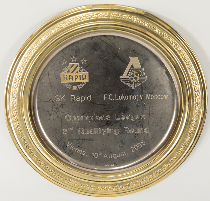 UEFA Cup 1989 Rapid Vienna v Club Bruegge Plate - Commemorative plate from Rapid Vienna marking the Champions League match "SK Rapid v FC Lokomotive Moscow Champions League 3rd Qualifying Round. Vienna, 10th August 2005" (engraving) (1:1), featuring the engraved logos of both clubs. Silver-plated metal plate with a gold-plated rim, 22 cm in diameter. Presented to UEFA observer Volker Roth on the occasion of this match. — Slight dent on the edge. Condition: A-