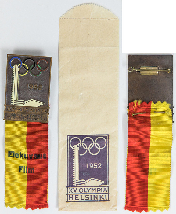  - Olympic Games 1952. Participant badge for "Film" (Cinematography) at the 1952 Helsinki Olympic Games. Bronze, with multi-colored enamel, featuring a printed violet silk ribbon. 11.5 x 3.3 cm. Includes: original paper packaging. --Rarity! Ebel 1952-5-059 --Excellent. EF. Condition: A-