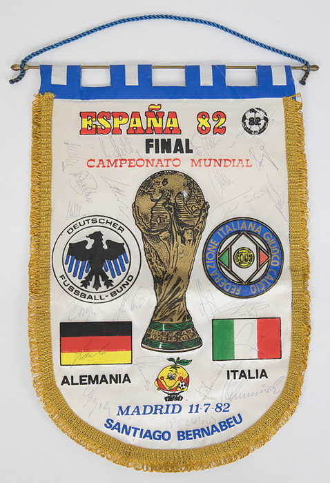Wimpel WM 1982  | Farbig bedruckter Souvenirwimpel "Espana 82 Final Campeonato Mundial Madrid 1-7-82, Alemania v Italia" mit 22 original Signaturen der deutschen Mannschaft die 1982 Fußball Vize - Weltmeister 1982 wurden, darunter Matthäus, Rummenigge, Fischer, Förster, H. Müller u.a. Mit rot-gelben Fransen, Metallstange und Seidenkordel. 41x30 cm.