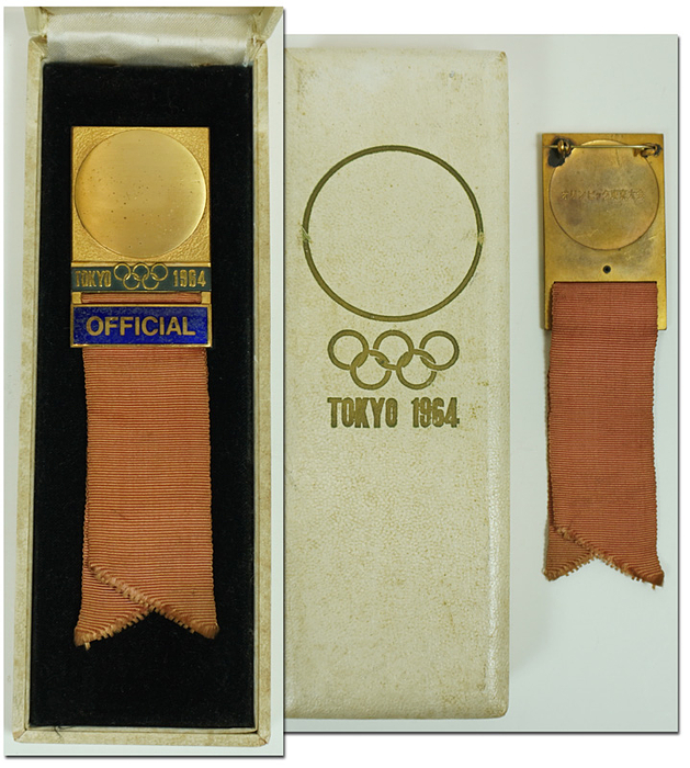 Offizielles Teilnehmerabzeichen Olympische Spiele Tokyo 1964 „Official“. Bronze, vergoldet. Schriftleiste blau emailliert. Sandfarbenen Seidenband. 14x3,8cm. In Originaletui.