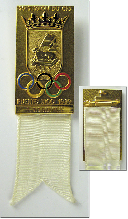 Offizielles Teilnehmerabzeichen für die "95. Session du CIO Puerto Rico 1989". Vergoldete Bronze mit weißem Seidenband für IOC-Mitlgieder. Mit eingraviertem Namen des Trägers "P. von Schoeller". 10x3 cm.