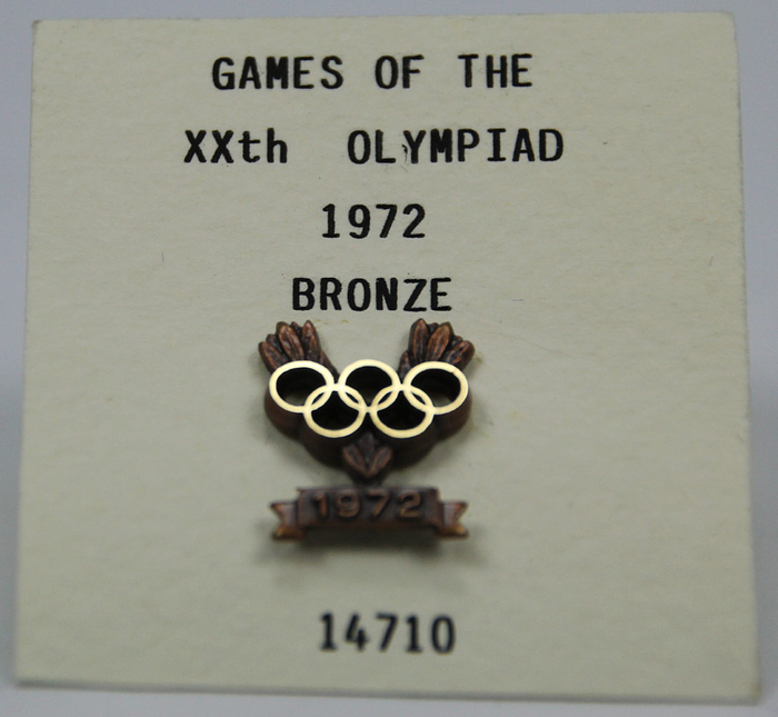Olympic Games 1972. IOC Bronze Medal Winner Pin - Official winner pin of the IOC from the Olympic Games in Munich 1972 from an Athlete, numbered "14710" for a bronze medal. Bronze, number "14710" engraved  on rear. Made by Bertoni, Milan. 2 x 1 cm. In original case. Since 1990 the IOC has awarded each Olympic medallist with an individual numbered pin. Silver medallists received silver pins, bronze medallists received bronze pins. Medallists of past Olympic Games received pins, too (partly posthumous) Condition: A
