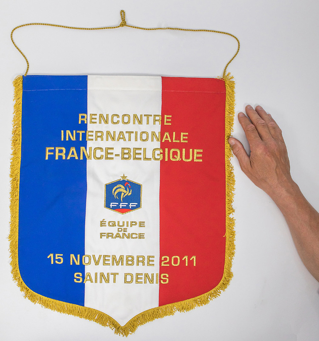 Frankreich-Spielwimpel 2011  | Offizieller Spielwimpel der Nationalmannschaft von Frankreich für das Freundschaftsspiel 2011 Frankreich v Belgien. Dreifarbiger Stoffwimpel mit gestickter Innschrift "Rencontre International  France - Begique. 15 novembre 2011 Saint Dennis" und aufgesetztem, besticktem Verbandsemblem von Frankreich. Mit gelben Seidenfransen und Seidenkordel. 48x43 cm.