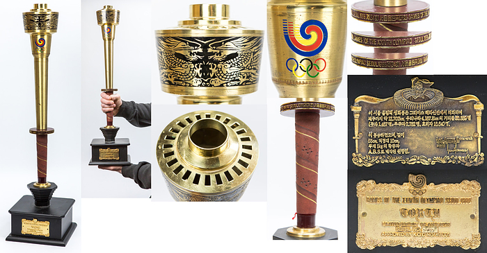 Olympic Games Seoul 1988 Original Torch - Original Olympic torch for the Seoul 1988 Olympic Games. Brass with leather handle with plastic shield (this one with the inscription "Games of the XXIVth Olympiad Seoul 1988"). Colored enamel Olympic logo and Olympic rings. Torch head with historical etched dragon motifs. 51cm. On an original black lacquered wooden base (17x17x13 cm) for this torch with a gilded bronze plaque with the inscription "Games of the XXIVth Olympiad Seoul 1988". Limited edition of 4167 sets. Serial number "No730 (hallmarked).  --Slight signs of wear (scratches) on the body. Otherwise very nice copy!!!. This torch with the base was offered directly from the manufacturer. The original torch is screwed to the base. --Slightly loosened Condition: A-