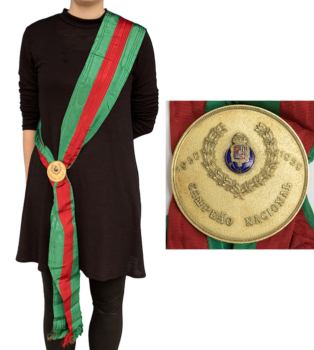 „Campeao Nacional 58-59“ offizielle Meisterschaftsscherpe in den Vereinsfarben des FC Porto mit Fransen aus Seide zusammengehalten von einer schweren Bronzeplakette mit aufgesetztem farbig emaillierten Vereinslogo. Gesamtlänge 220 cm x 13,5 cm. Durchmesser der Plakette 6,5 cm. Persönliches Exemplar von der Trainerlegende BELA GUTMANN (1899-1981) der 1959 den Meistertitel gewann, bevor er zu Benfica Lissabon wechselte. Mit Benfica gewann er 1961 und 1962 den Europapokal der Landesmeister. Status:AAA.