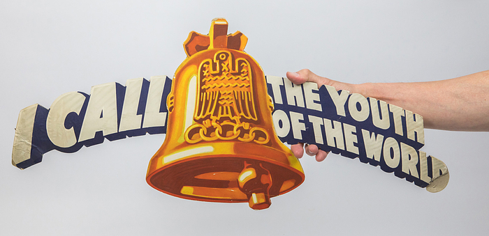 Englischsprachiges Werbeschild zu den Olympischen Spielen 1936 "I call the youth of the world" (Ich rufe die Jugend der Welt). Pappschild mit Aufhänger, 70x31 cm.