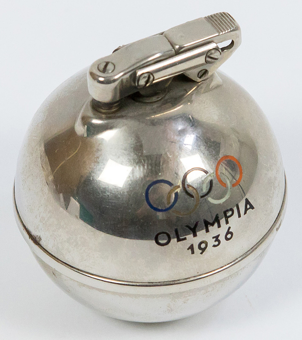 Feuerzeug 1936  | Verchromtes Feuerzeug in Kugelform mit farbigen emaillierten Olympischen Ringen und der Inschrift "Olympiade 1936". 6x4,5 cm cm.