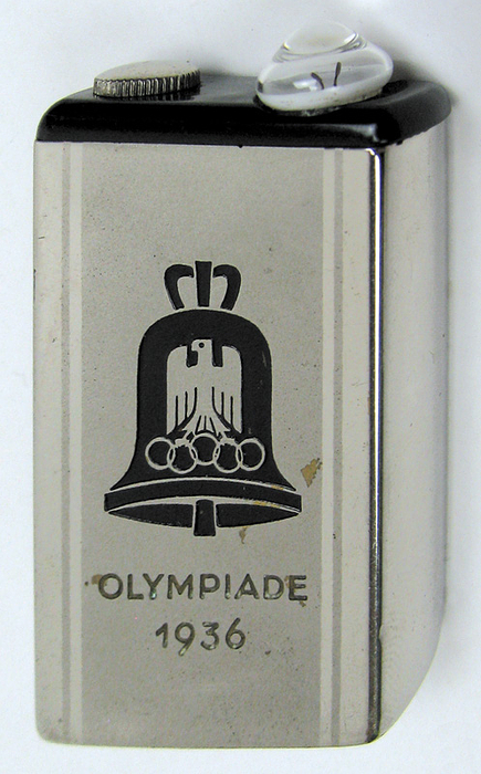 Taschenlampe 1936  | Verchromte Taschenlampe mit eingravierter Olympiaglocke und Schriftzug „Olympiade 1936“. 6,2x3,2x1,7cm.