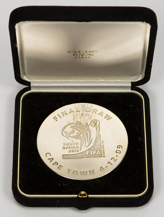 „FIFA World Cup South Africa 2010. Final Draw Cape Town 4 - 12- 09“ Offizielle Teilnehmermedaille der FIFA für die Auslosung zur Fußball-Weltmeisterschaft. Bronze, versilbert mit vergoldetem World Cup. 6,0cm. Im original Etui.