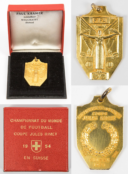 Offizielle Siegermedaille der FIFA für die ungarische Mannschaft für den 2.Platz bei der 5.Fußball-Weltmeisterschaft 1954 in der Schweiz. „Championat du Monde Coupe Jules Rimet Suisse 1954" Silber, vergoldet (gestempelt, 925er Silber.  Hersteller: "PEKA"), 3,6x2,3 cm. Im original Pappetui mit goldgeprägtem Deckel und Pappscharnier (5,5x5,5x1,4 cm).