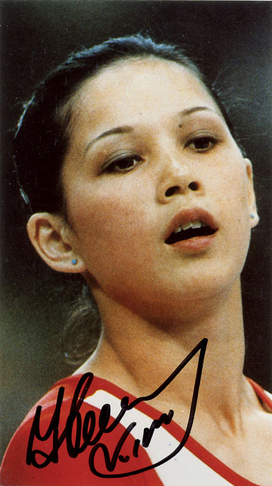 Farbreprofoto mit Originalsignatur der fünffachen Goldmedaillen-Gewinnerin  der Olympischen Spiele 1976 + 1980 im Turnen Nelli Kim (URS) + Silber 1976. 13,5x7,5 cm.