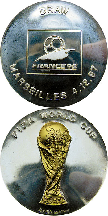 „FIFA World Cup“ Silbermedaille mit aufgesetztem goldenen Weltpokal. Rückseite: „Draw Marseille 4.12.97“. Teilnehmermedaille für die Auslosung der Endrunden-Gruppen der Fußball-Weltmeisterschaft 1998. Bronze, versilbert, 6,0cm. In original Etui.