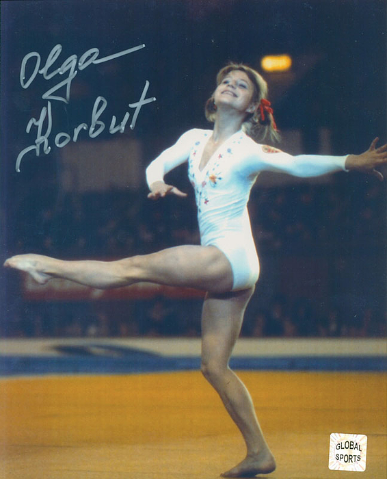 Farb-Pressefoto mit original Signatur von Olga Korbut (URS). Vierfache Goldgewinnerin der UdSSR bei den Olympischen Spielen 1972 und 1976 im Turnen. 25x20 cm.