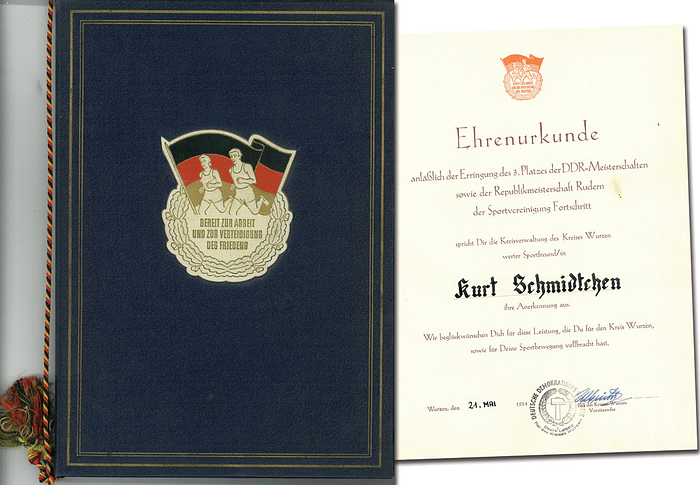 "Ehrenurkunde abläßlich der Erringung des 3.Platzes der DDR - Meisterschaften…Rudern ..(für) Kurt Schmidtchen….21.Mai 1954". In original Urkundenmappe mit geprägtem, farbigen Logo "Bereit zur Arbeit und zur Verteidigung des Friedens" und schwarz-rot-goldenes Seidenbändchen, 32,5x23 cm.