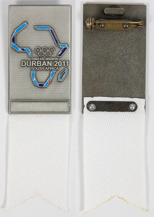 Offizielles Teilnehmerabzeichen für die 123. IOC Session 2011 Durban South Africa. Zinklegierung, farbig emailliert, mit weißem Seidenband. Zusätzlich weiße original Kordel. 10x3 cm. In original Verpackung.