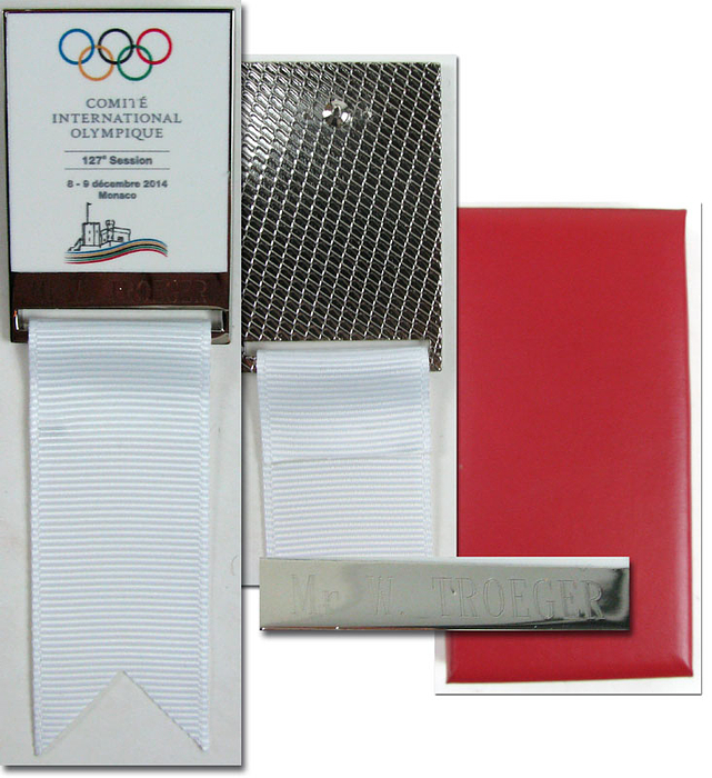 Offizielles Teilnehmerabzeichen für die 127. IOC Session Monaco 2014. Vergoldet, farbig emailliert, mit weißem Seidenband. 11x3,1 cm.