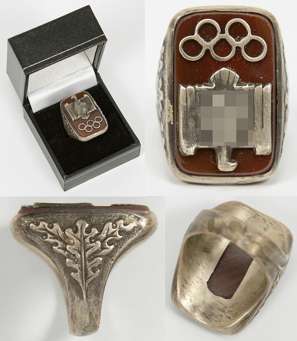Massiver Silberring. Mit aufgesetzten silbernen Olympischen Ringen und einem Reichsadler mit Hakenkreuz montiert auf einem Bernsteinplättchen. Ring an den seutlichen Ringschienen mit Eichenblättern verziert. Silber (gepunzt 835er, Gewicht 20 Gramm). 3x2x2,5 cm.