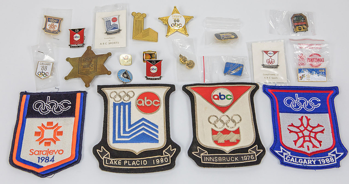 Sammlung eines ABC (American Broadcasting Company) Reporters von den Olympischen Spielen 1972 bis 1988. 17 Pins und badges (7,5x6,3 cm bis 1,1x1,1 cm) und 4 großen Stoffabzeichen (12x10 cm).