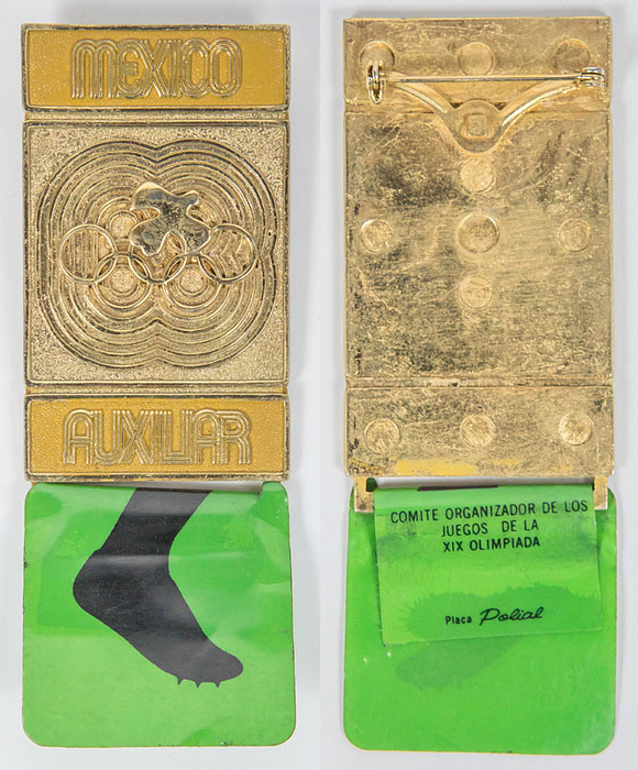Teilnehmerabzeichen Olympische Sommerspiele Mexico 1968 „Auxiliar“  für Helfer. Bronze, vergoldet, orange emailliert. Mit grünem Plastikschild für Leichtatheltik. 10x3,5 cm.