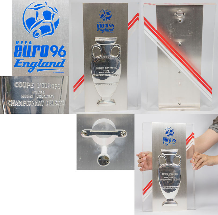Große offizielle Teilnehmerplakette für die Fußballverbände die an der Endsrunde der UEFA EURO 1996 in England teilgenommen haben. Jeder teilnehmende Landesverband erhielt eine dieser Plaketten. Massiver Plexiglaswandplakette mit eingelassener Edelstahlplatte mit einem geprägtem Siegerpokal der UEFA Euro. Außerdem ein blau emailliertes offizielles Logo der UEFA Euro 1996 in England. Auf der Rückseite der Plakette sind rot-weiß Streifen, die Farben des englischen Fußballverbandes, aufgetragen. Gewicht: 5,8 Kg. 40x24x4 cm.