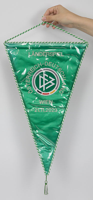 Original Spielwimpel des DFB für das Länderspiel Österreich - Deutschland (2:0) am 21.11.2023 in Wien. Grüne Seide mit silberbrokat aufgesticktem Schriftzug und aufgesetztem geticktem DFB Logo. Mit Grün-weißer Seidenbordüre. In original Kunststoffschutzhülle. Größe: 48x30,5 cm. (ohne Bommel).