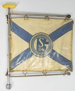 Original Fahne von Schalke 04 von der Siegesfeier zur letzten Deutschen Fußballmeisterschaft 1958. Autostander aus verchromten Metall und einer Kunststoffmontierung. In den Halterungsringen eine Seidenfahne mit aufgesetztem bedrucktem Logo von Schalke 04. Mit blauen aufgenähten Leinenstreifen. Alles beidseitig. Die Fahne befindet sich in einer original Plastikhülle, die die Fahne vor Fahrtschmutz schützen sollte. 30x24 cm. - Bild 2