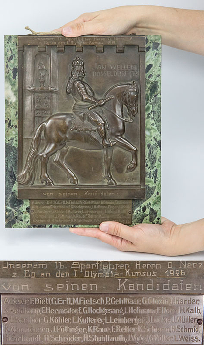 Wandplakette für den ersten deutschen Reichstrainer (Bundestrainer) der deutschen Nationalmannschaft. Geschenk von den deutschen Nationalspielern anläßlich des ersten Sichtungslehrgang 1926. Mit der Inschrift "Unserem lb. Sportlehrer Herrn O.Nerz z. Eg. An den I. Olympia Kursus 1926" "von seinen Kanditaten". Alle graviert auf einer großen Bronzetafel (24x19 cm) des Düsseldorfer Bildhauers Wieh. Darunter eine Bronzeplakette mit den gravierten 31 Namen der Spieler des ersten Sichtungslehrganges 1926. Beide Stücke auf Marmorplatte montiert. Gewicht: 4 kg. 29x23,5 cm UNIKAT!!!.