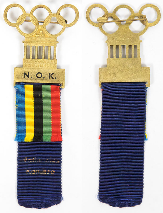 Offizielles Teilnehmerabzeichen „N.O.K.“ Für die Präsidenten der Nationalen Olympisches Komitees für die Olympischen Spiele Berlin 1936. Bronze, vergoldet. Mit kurzem Band in den olympischen Farben und langem blauen Band mit goldenem Aufdruck „Nationales Komitee“, 11x4,1 cm.