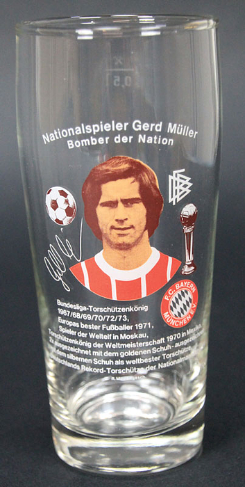 Dekoratives, farbig bedrucktes Glas „Nationalspieler Gerd Müller. Bomber der Nation" mit Porträt und Auflistung aller Erfolge bis 1973, DFB-Logo, Torschützenpokal und Bayern-München Vereinslogo. Füllmenge 0,5 l, Höhe 17,5 cm. Hergestellt ca. 1974.