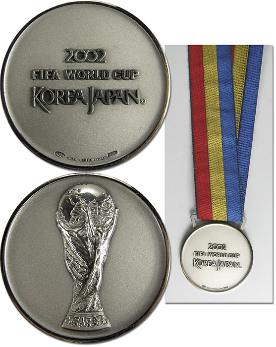 Offizielle Siegermedaille der deutschen Mannschaft für den 2.Platz bei der Fußball-Weltmeisterschaft 2002 in Korea Japan. "2002 FIFA World Cup Korea Japan“ Silber (gepunzt, 925er Silber), vergoldet an original, dreifarbigem Seidenband. Hersteller: Bertoni. 5 cm.