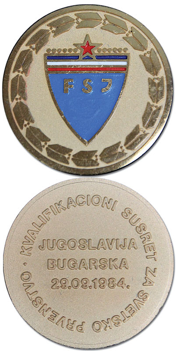 Teilnehmermedaille für Spieler der Nationalmannschaft von Jugoslawien für das Länderspiel Jugoslawien v Bulgarien am 29.09.1984 mit der Aufschrift "Jugoslavija - Bugaraska 29 09.1984". Vorderseite der Medaille mit farbig emailiierten Verbandslogo von Jugoslawien. Tomak, vergoldet, 5 cm. In original Box.