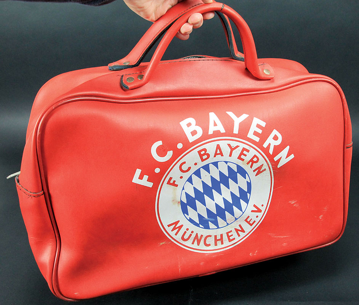 Rote Souvenir Sporttasche it der Aufschrift "F.C. Bayern" und einem großen aufgedruckten Vereinsemblem des FC bayern München. Ca. 1975. Kunstleder, 48x30x16 cm.