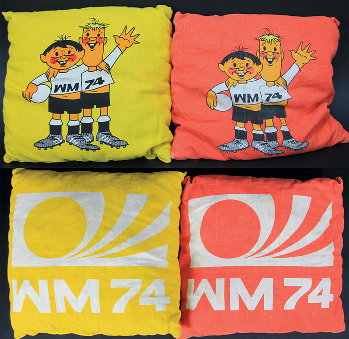 Zwei Kissen in gelb und rot mit den WM 1974 Maskottchen Tip und Tap. Auf der andernen Seiten offizielles Logo der Fußball-Weltmeisterschaft 1974. Leinen mit Polyesterfüllung, 35x35 cm.
