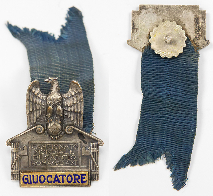 "Campionato mondiale di Calcio Rom 1934 XII" Nummeriertes offizielles Teilnehmerabzeichen Fußball-Weltmeisterschaft 1934 Italien „Giuocatore“ (Spieler). Bronze, versilbert, Schriftleiste blau emailliert. Mit eingravierter Nummer auf der Rückseite "125". Hersteller: Picchiani, Barlacchi, Firenze. With blauen Seidenband. 4,3x3,6 cm.