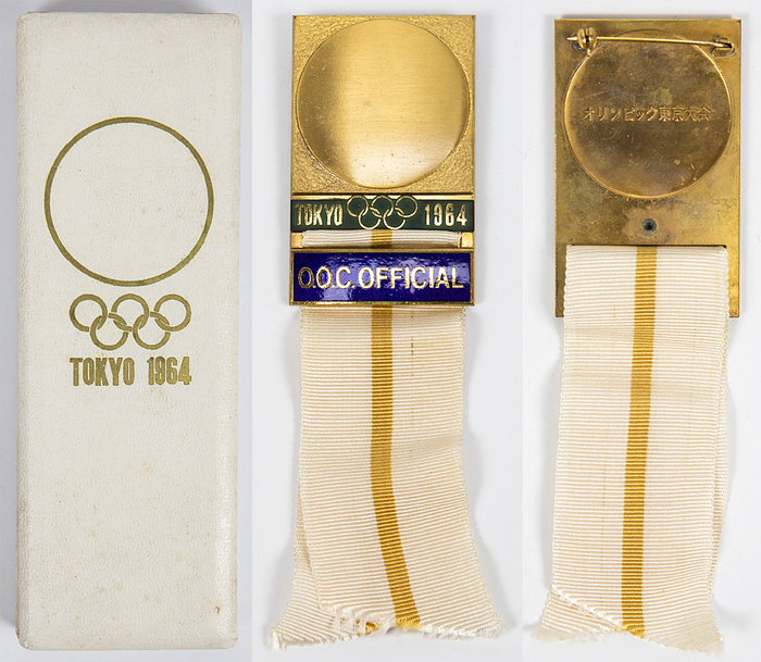 Offizielles Teilnehmerabzeichen Tokyo 1964 „O.O.C. Official“. (Olympic Organisation Comittee). Bronze, vergoldet. Schriftleiste blau emailliert. Seidenband in weiß-gelb. 14x3,8cm. In Originaletui.