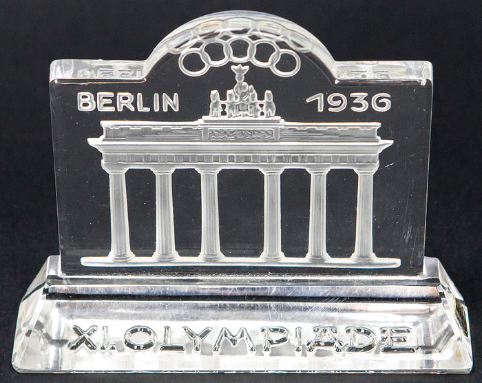  - Paperweight made of Bohemian lead crystal glass commemorating the XI Olympiad Berlin 1936. Motif: Brandenburg Gate with Olympic rings. Inscription "XI. Olympiade" on the base. 14 x 12 x 3 cm. --A very rare and decorative memento of the 1936 Berlin Olympic Games in mint condition! Condition: A