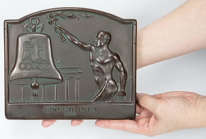  - Large torch relay plaque "Olympic Games 1936". Featuring torchbearer, Brandenburg Gate and the Olympic Peace Bell. Fired plaster, brown lacquered. 19.5 x 17 cm. --Very nice wall plaque. With small chips. Condition: B