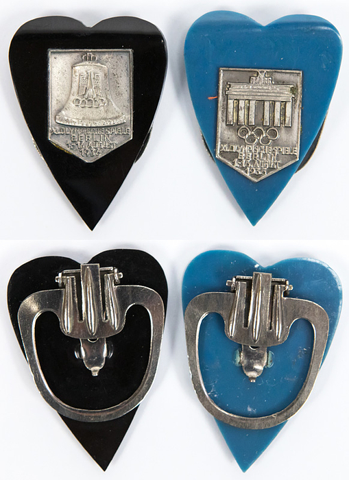 Klip OS1936  | Zwei herzförmige Clips aus schawrzem und blauen Bakelit mit versilberten aufgesetzten Plaketen mit verschiedenen Olympischen Motiven und der Aufschrift "XI. Olympische Spiele Berlin 1936". Klips aus Metall, je 4,5x3,3 cm.