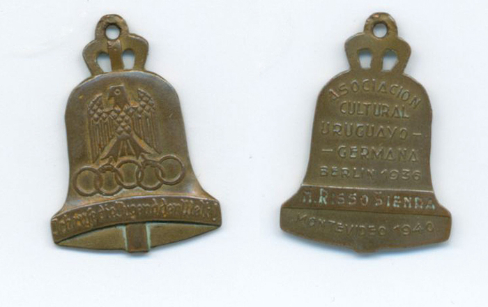  - Small plaque "Olympic Bell" of the 1936 Berlin Olympic Games. With the inscription "Association Cultura Uruguay - Germania Berlin 1936 Montevideo 1940" on the reverse, along with engraved names. Bronze, 3.1 x 2.3 cm --A very rare commemorative plaque issued to participants of a German delegation's visit to Uruguay in 1940. The German-Uruguayan Society was founded in 1936 on the occasion of the Olympic Games in Berlin. Condition: A