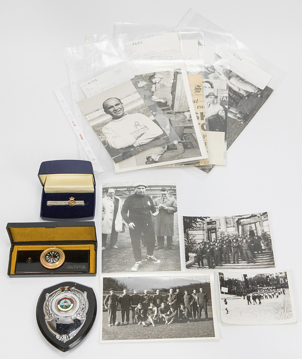  - Various items documenting Bela Guttmann's career from 1945 to 1966: 1) Original black and white photograph of a celebration in Bukrest with the A.S. Ciocanul Bucharest team, 1945. 12x9 cm. Guttmann only managed two victories against the rival of the club president, but he immediately became Bucharest city champion, which in 1945 was equivalent to the national championship. 2) Hungarian winner's plaque, circa 1948, Bekalit, silver-chrome-plated shield, partially enameled, 13x9 cm. 3) Two original  black and white press photos: "Bela Guttmann explains his tactical concept to the Trieste team," 1952. 23x16 cm. 4) Two original black and white photos: "Team photo" and "The coach," Bela Guttmann of Lanerossi Vicenza, 1955/56. 14x10 cm. After being dismissed by AC Milan, he took over as coach of relegation-threatened Lanerossi. Under Guttmann, the heavily favored relegation candidate finished in mid-table and held AC Milan's San Siro stadium to a 0-0 draw. 5) Original black and white press photo "Exile team of Honved Budapest in Barcelona". 1956. 18x11 cm. 6) 3 original black and white press photos "Bela Guttmann at Servette Geneva" 1966. 18x12 cm. At 67, the "miracle doctor" took over as coach of Servette. 7) Gold-plated car clock with black dial. Mounted on a plastic console with gold logo and inscription "Real Federacion Española de Futbol". In original presentation box. Circa 1970. 12x4.5 cm. Clock is fully functional, with a mechanical movement. Gift from the Spanish Football Federation to Guttmann 8) Tie pin of the Spanish Football Federation, circa 1964. - Guttmann Estate 2001 Nos. 154, 155, 164, 181, 187, 255, 276, 295 Condition: A-B