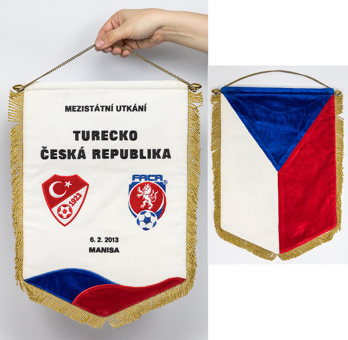  - Official match pennant of the Czech national football team for the international match against Turkey, featuring the silk-embroidered inscription "Turecko - Ceska Republika, 6.2.2013, Manisa". With gold brocade fringe and embroidered logos of both federations. Brass rod and chain. 41 x 28 cm --This pennant was awarded to Türkiye and the referees. The pennant came from one of the referees of this match. Condition: A-