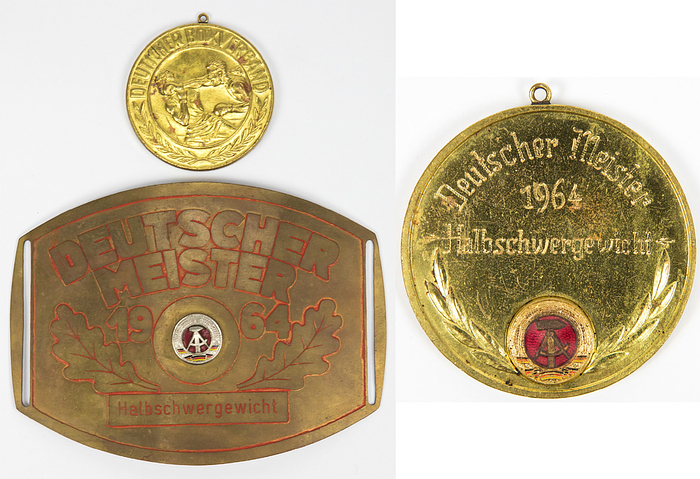Meistergürtel DDR Boxen 1964  | Original Gürtelschnalle für Bernd Anders (TSC Berlin) den DDR Meister im Boxen mit der Aufschrift "Deutscher Meister 1964 Halbschwergewicht". Messing, mit geröteten Linien und aufgesetztem farbig emaillierten DDR-Staatswappen, 15x11 cm. Dabei die dazugehörige Siegermedaille für den DDR Meister 1964 des Deutschen Boxverbandes mit rückseitiger Gravur "Deutscher Meister 1964 Halbschwergewicht". Bronze, vergoldet mit aufgesetztem emaillierten Staatswappen, 6 cm.